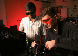 Researchers in goggles stare at a monitor with red light in the background