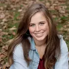 Happy young woman with long brown hair and blue eyes, wearing a light blue denim jacket and dark red top, with autumn leaves.