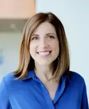 Smiling woman with brown hair, wearing a blue button-up shirt.